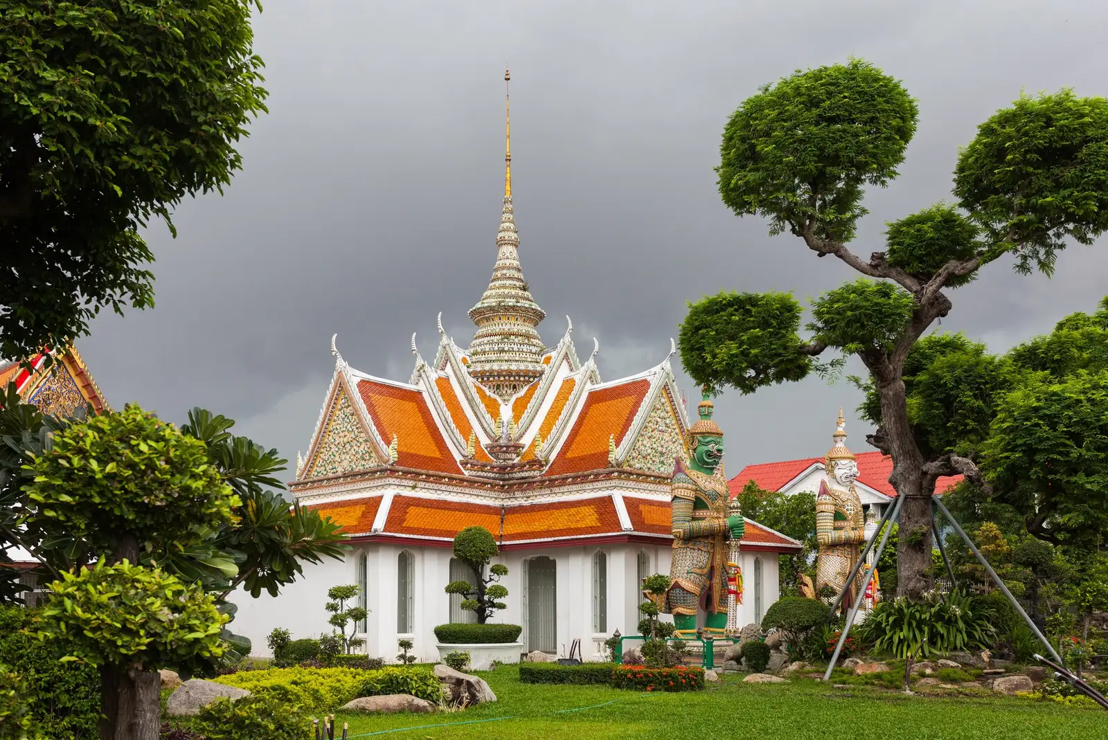 Una cappella di Wat Arun con i tetti arancioni fra gli alberi potati