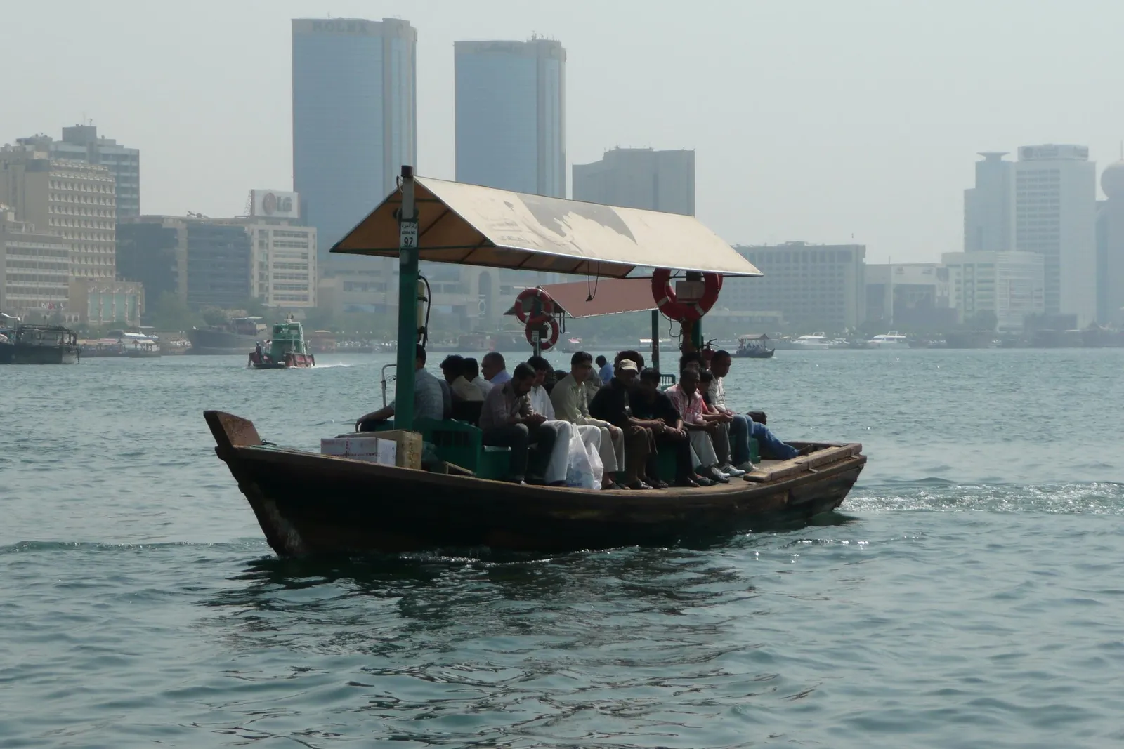 An abra full of passengers on Dubai Creek, with buildings behind