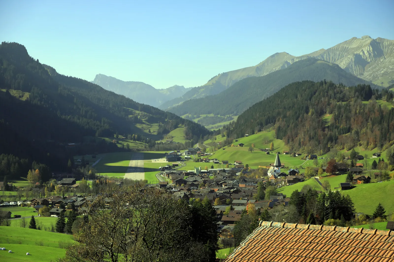 The valley from Gruben station: Saanen and its church on the valley floor beside the airfield runway, among green slopes and mountains