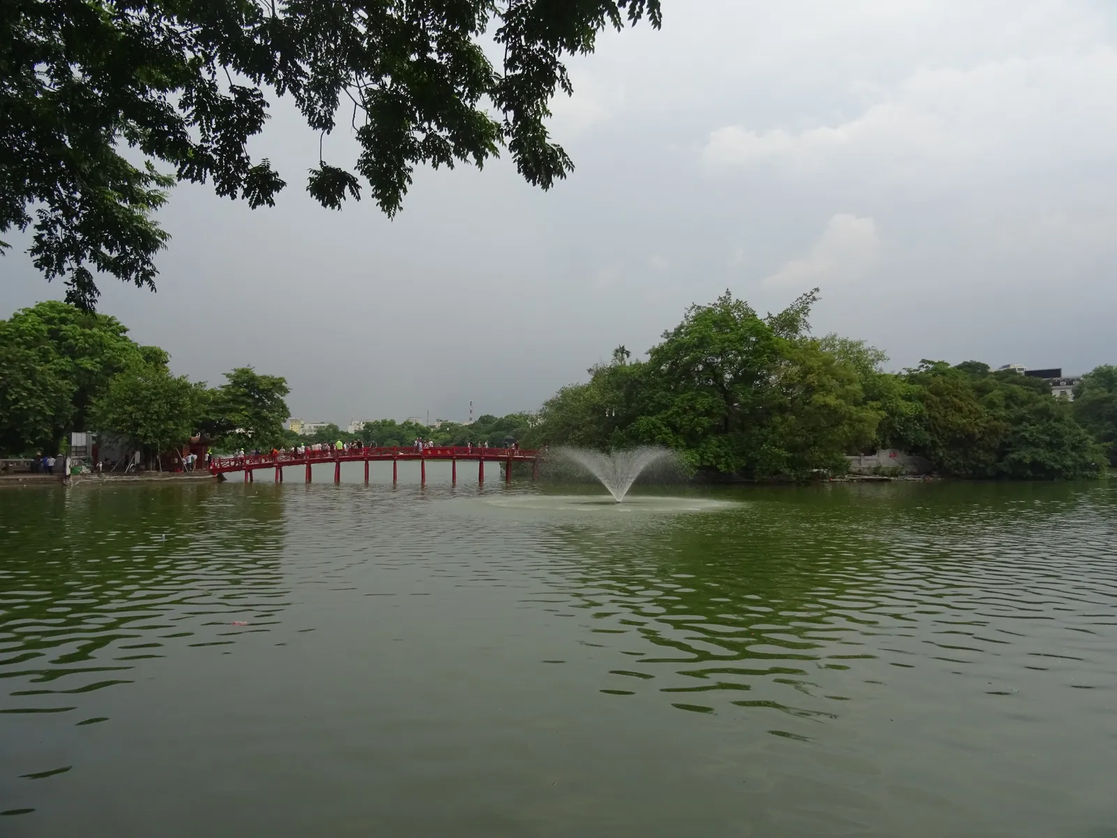 Hoan Kiem Lake with a fountain, the red bridge and Ngoc Son Temple among the trees