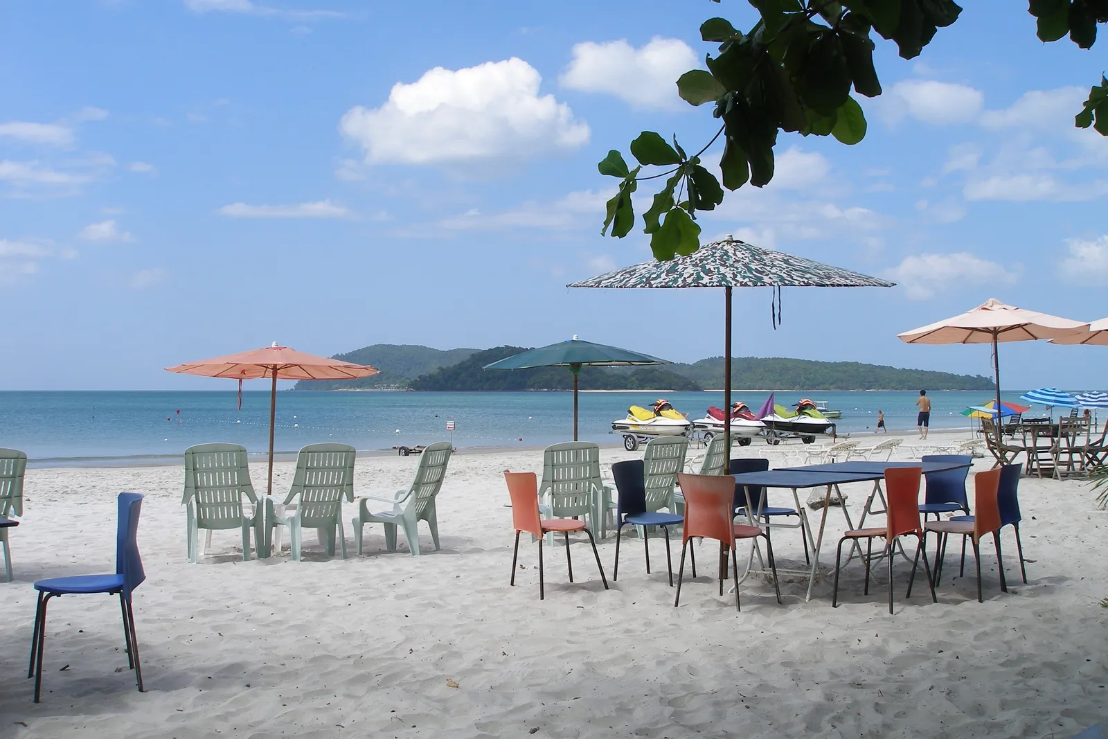 Tables and parasols on the white sand of Pantai Cenang, the sea and islands beyond