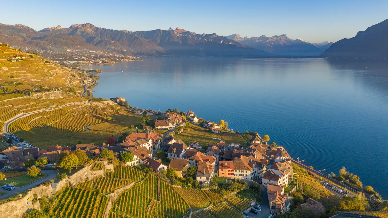 The Lavaux vineyard terraces from the air in autumn colours: a village among the vines running down to Lake Geneva, with the Alps behind