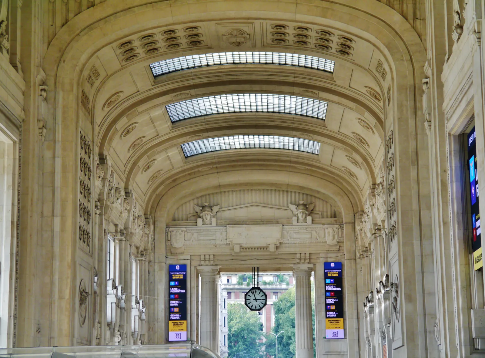 The Galleria delle Carrozze inside Milano Centrale, with its vault, skylights, departure boards and a clock under the arch