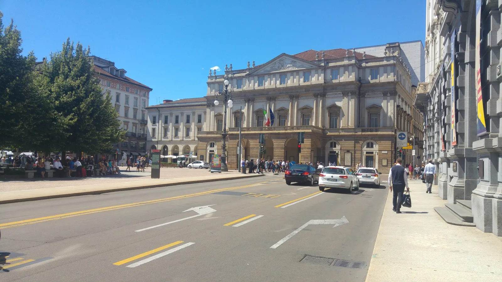 The neoclassical facade of Teatro alla Scala seen from the street, with cars and passers-by