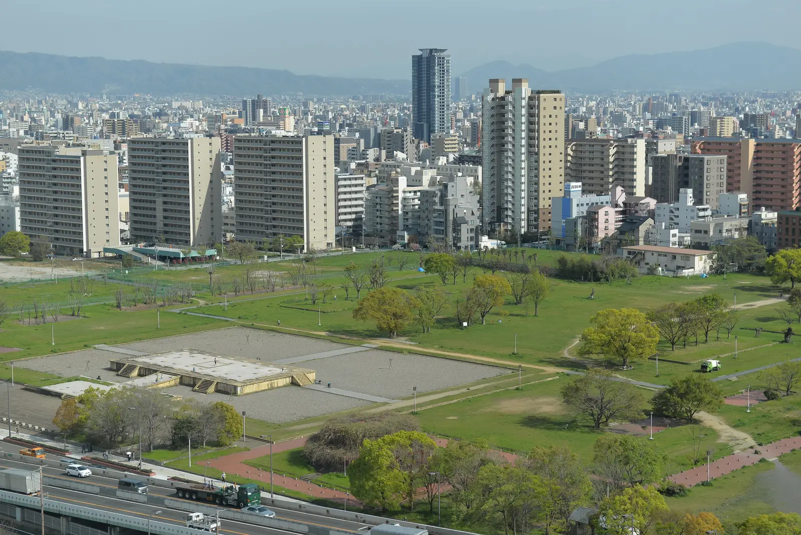 The lawns and low platforms of the Naniwa palace site seen from above, the city’s towers behind