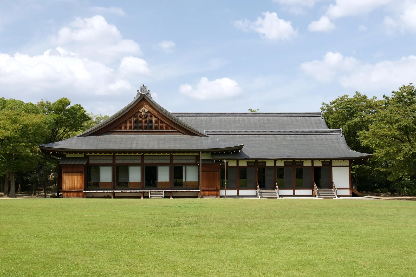A wide lawn in the Nishinomaru Garden, a low traditional building and trees behind