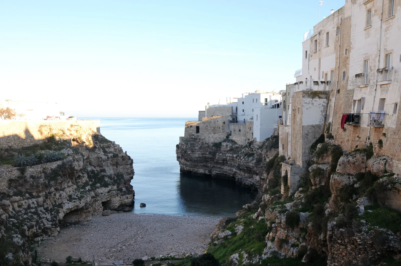 Lama Monachile in Polignano a Mare: a pebble cove between rock walls, with houses on the cliff edge and the open sea beyond.