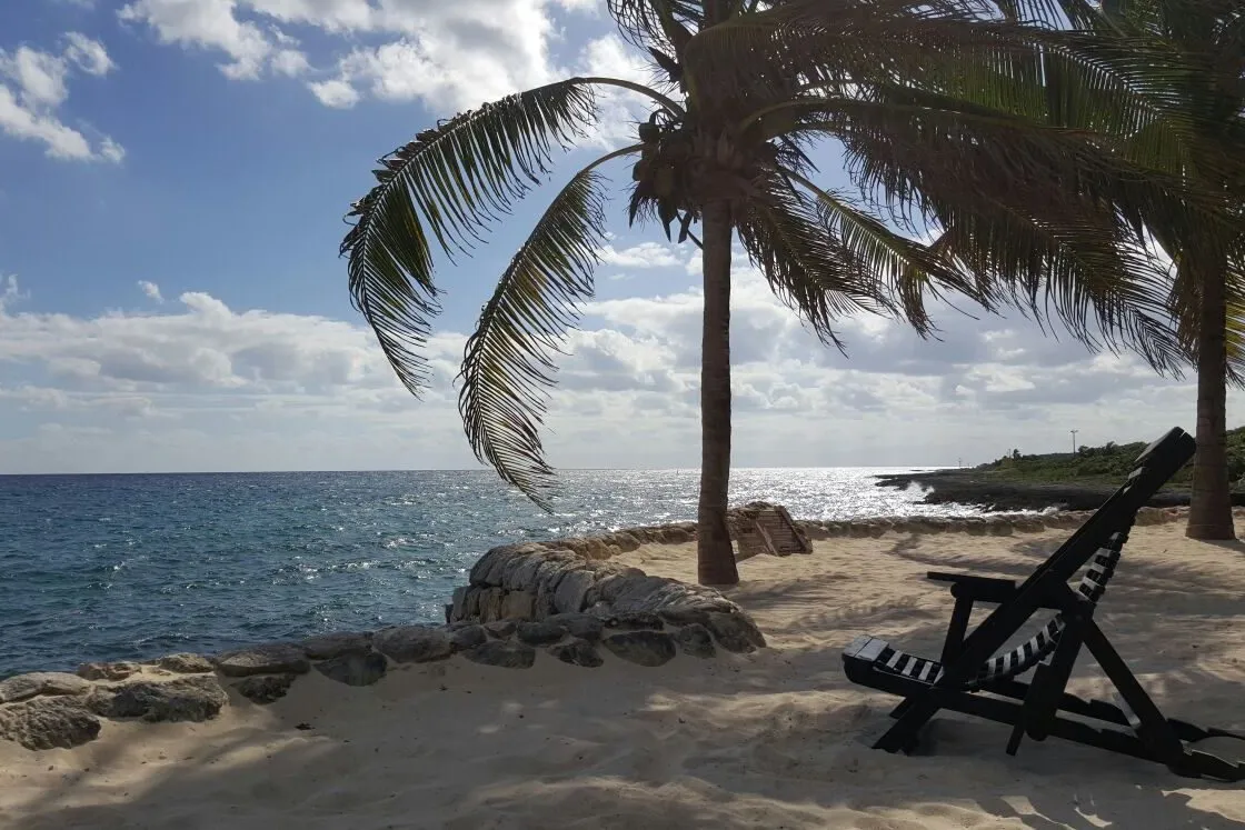 The beach at Xcaret park, palms and a wooden lounger on the sand by the sea