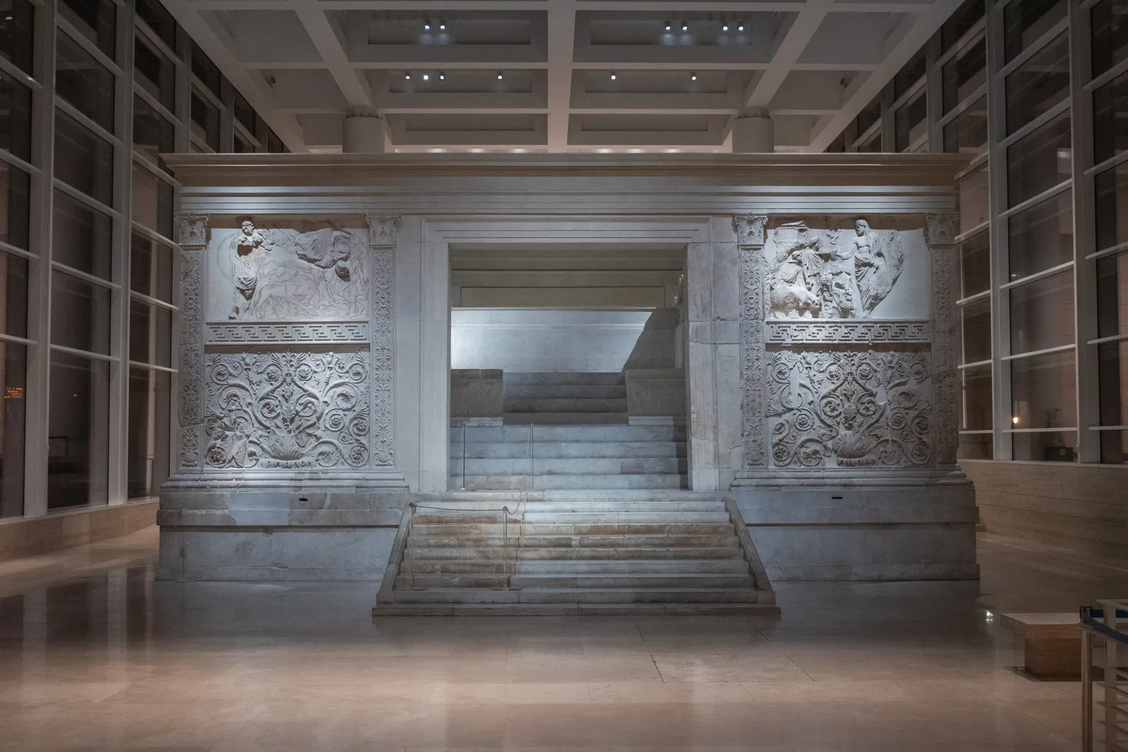The Ara Pacis from the front inside Richard Meier’s pavilion: the white marble enclosure carved with reliefs and scrolls, the central steps and the glass walls, lit in the evening.