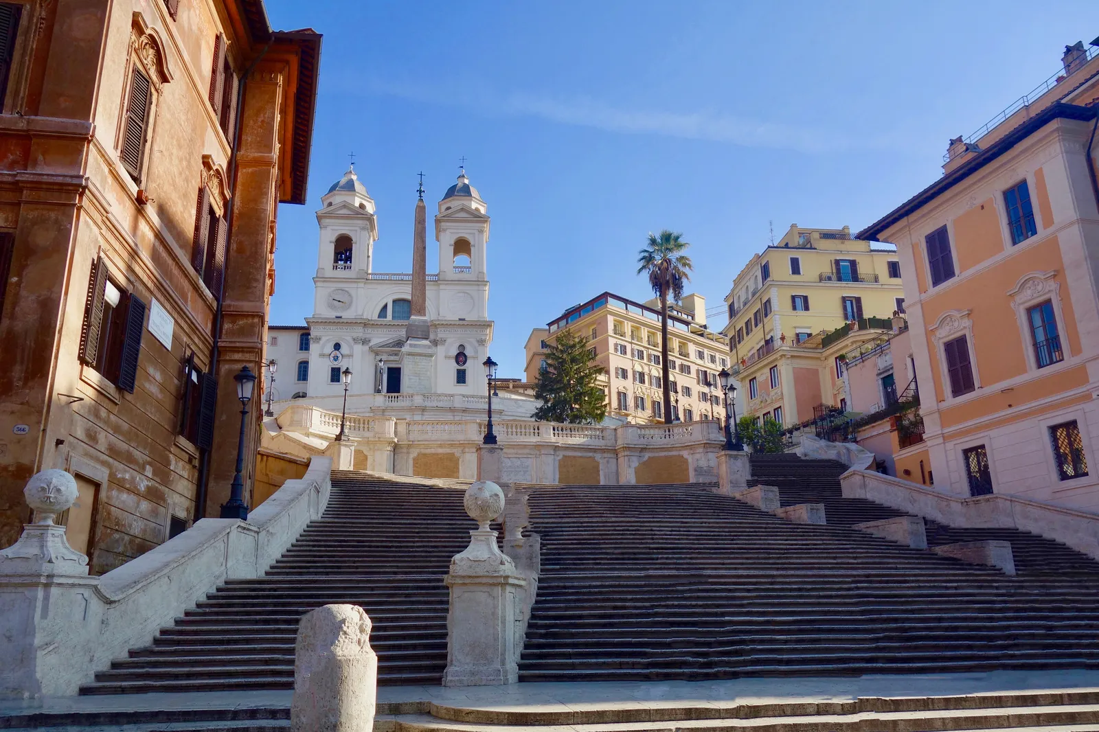 The Spanish Steps empty in the morning light, rising to the church of Trinità dei Monti with its 2 bell towers and the Sallustiano obelisk, between ochre and pink palazzi.