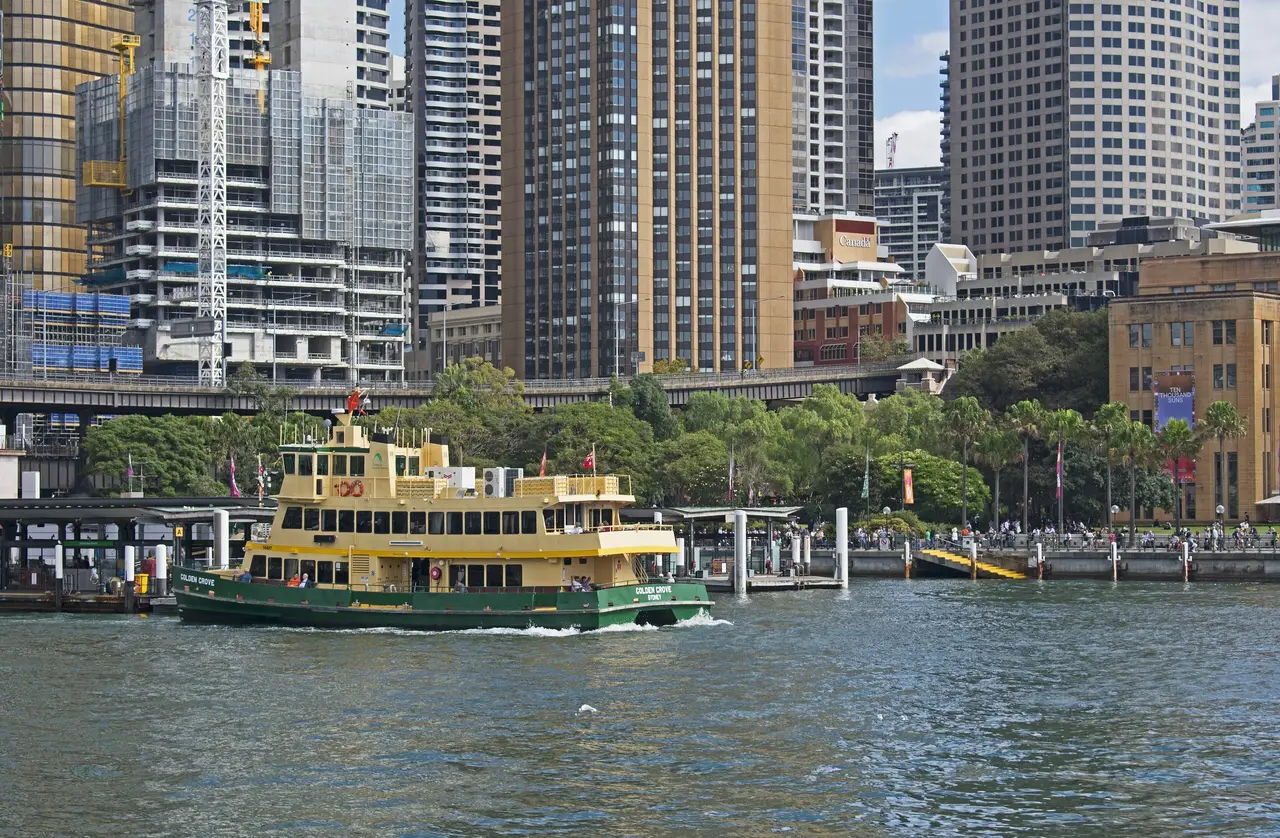 A green-and-yellow ferry at a Circular Quay wharf, the city’s towers behind