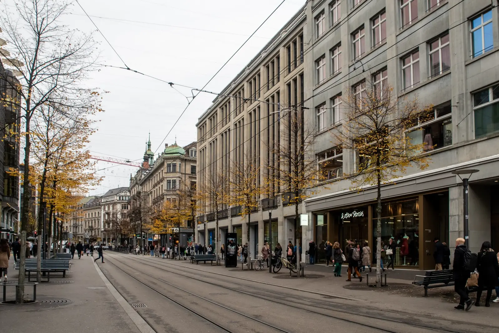 Bahnhofstrasse in autumn: tram tracks, trees turning yellow and shoppers under stone façades