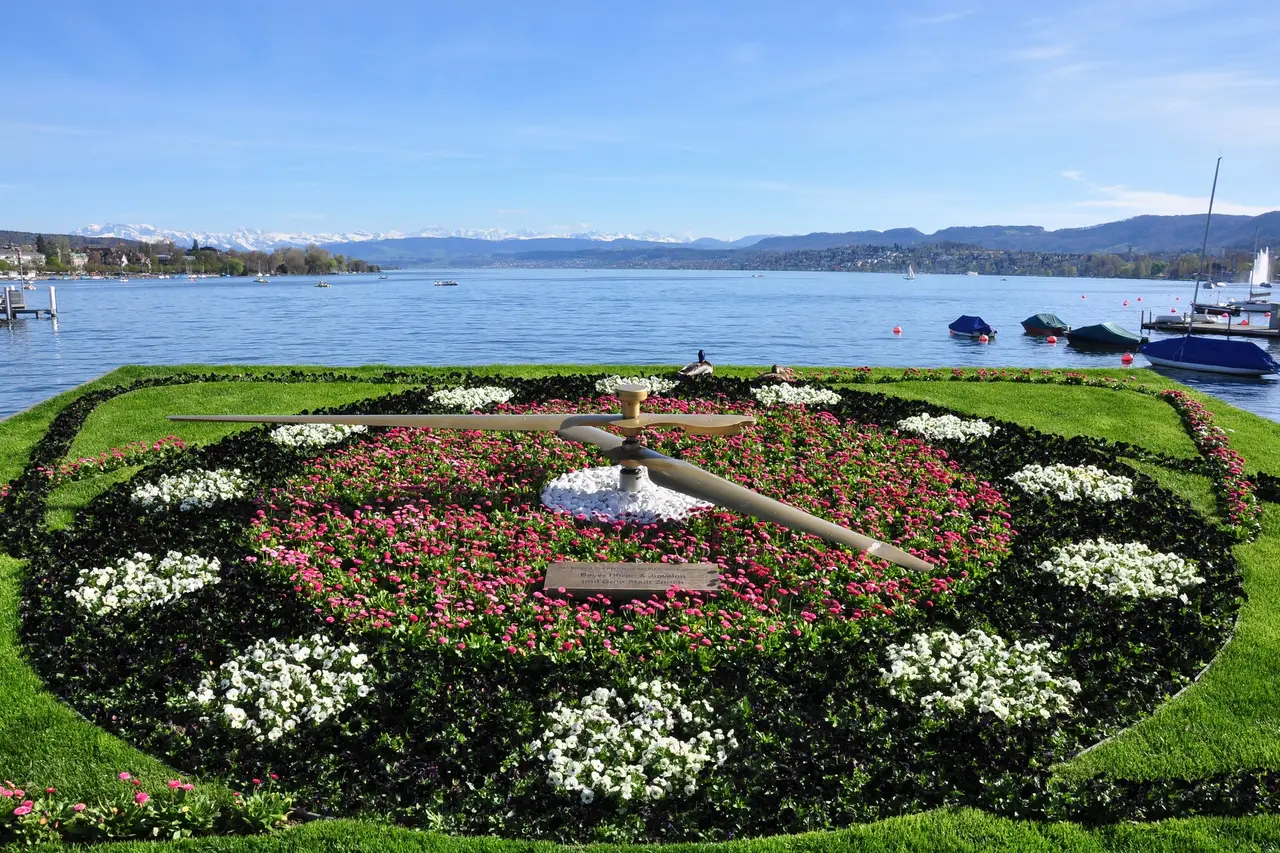 Bürkliplatz on the lake shore: the flower clock in pink and white, boats on Lake Zurich and the snowy Alps on the horizon