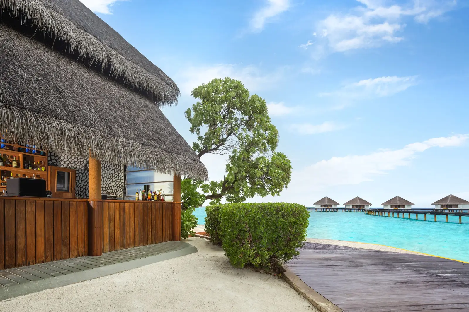 A thatched bar on the shore and, beyond it, the water villas in the turquoise lagoon