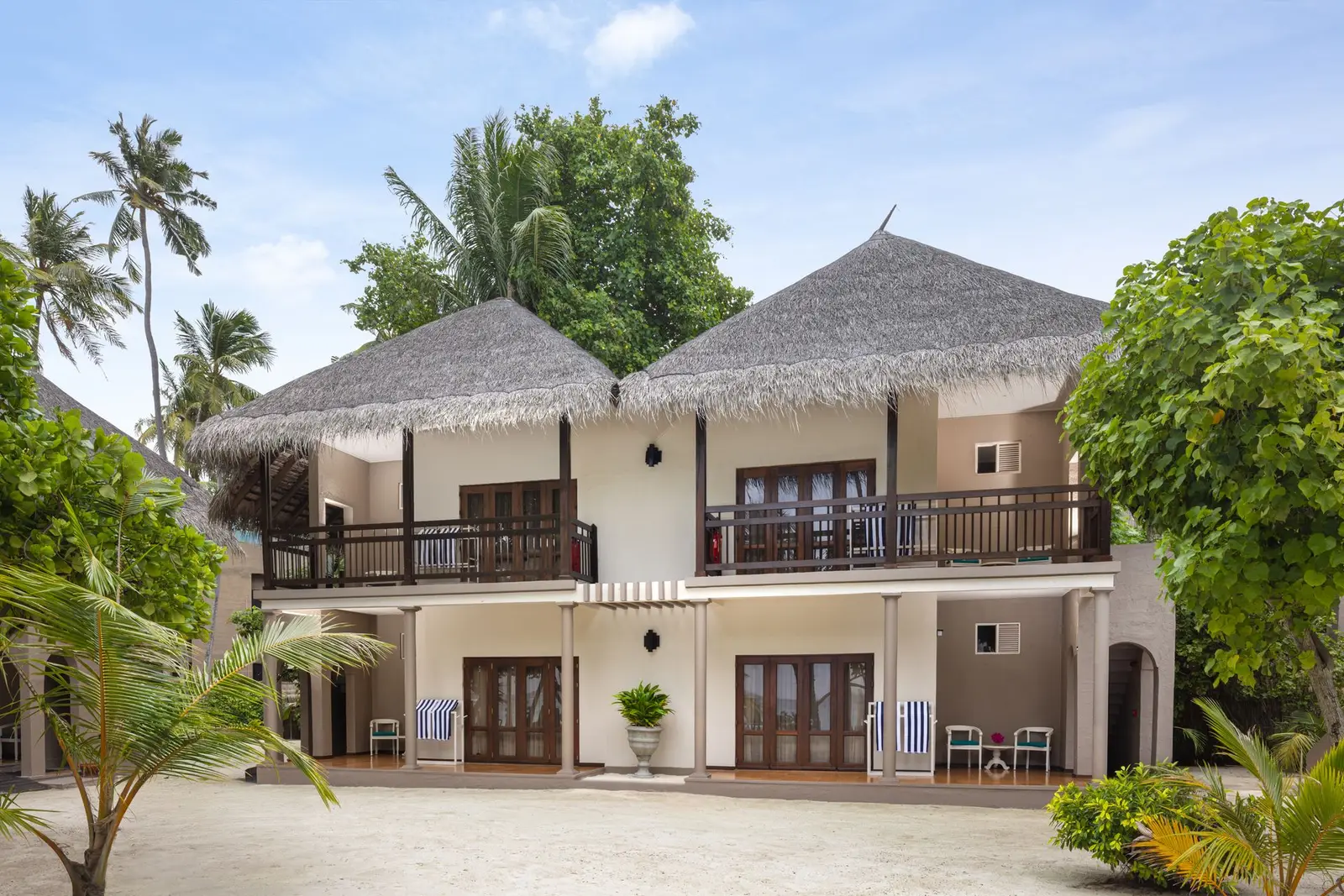 A 2-storey thatched block among the palms, balconies above and doors on to the sand below
