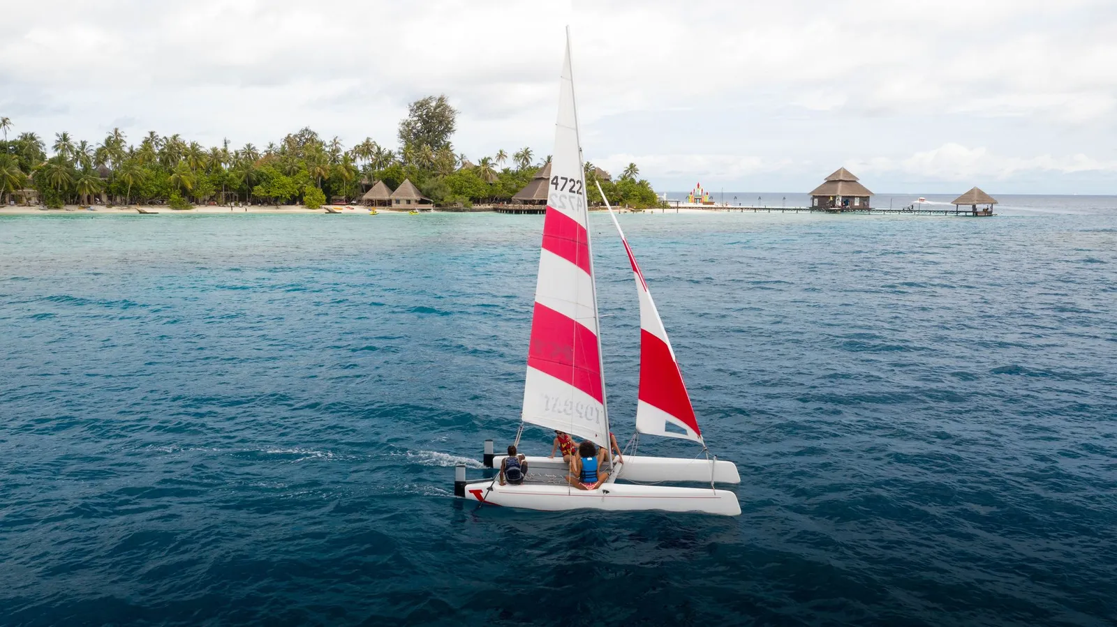 A catamaran with a red and white striped sail off the island