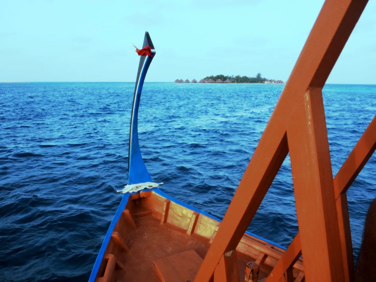The bow of a dhoni on a deep blue sea, a low island on the horizon