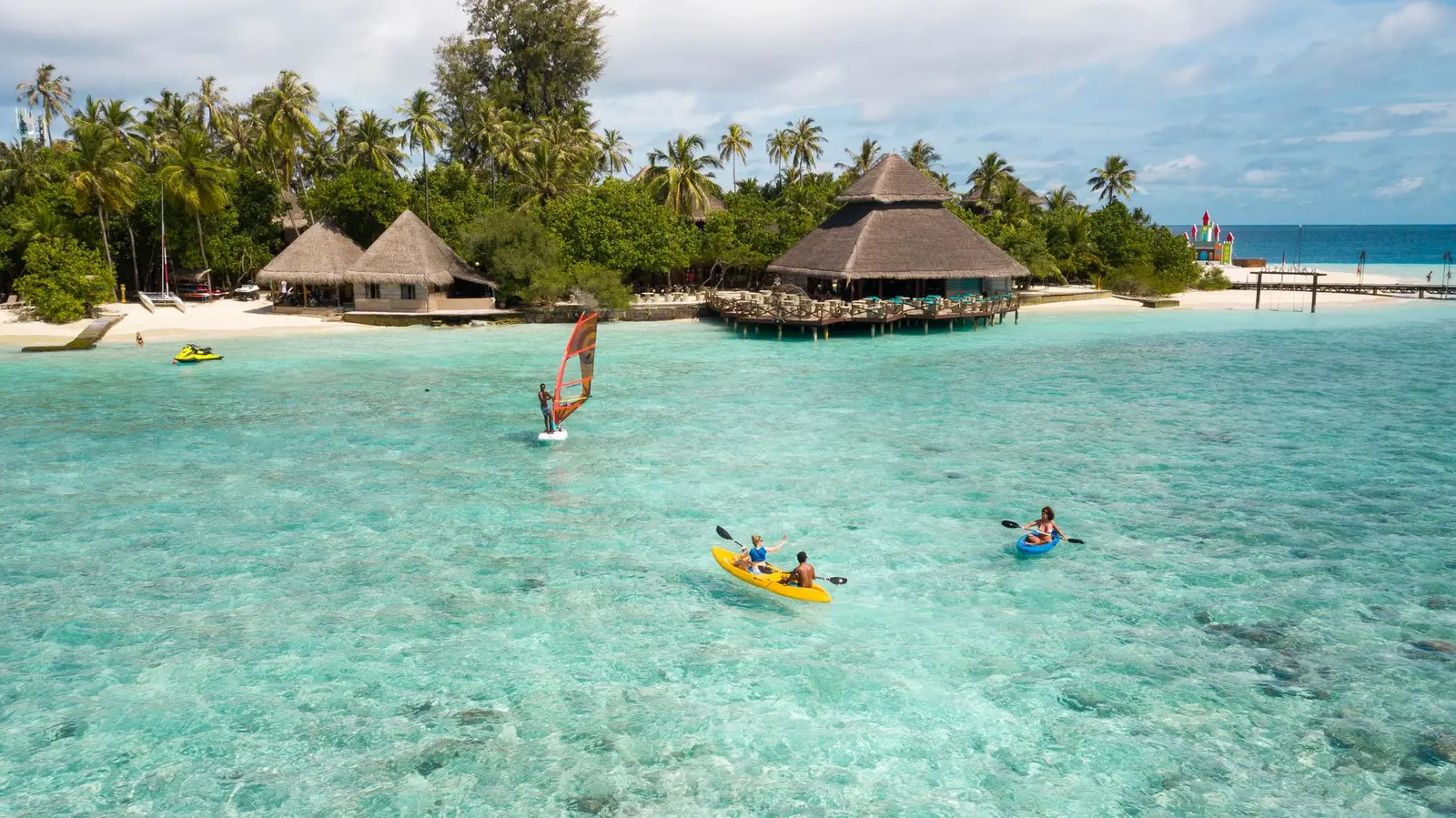 Kayaks and a windsurfer in the shallow lagoon off the beach and the thatched pavilions
