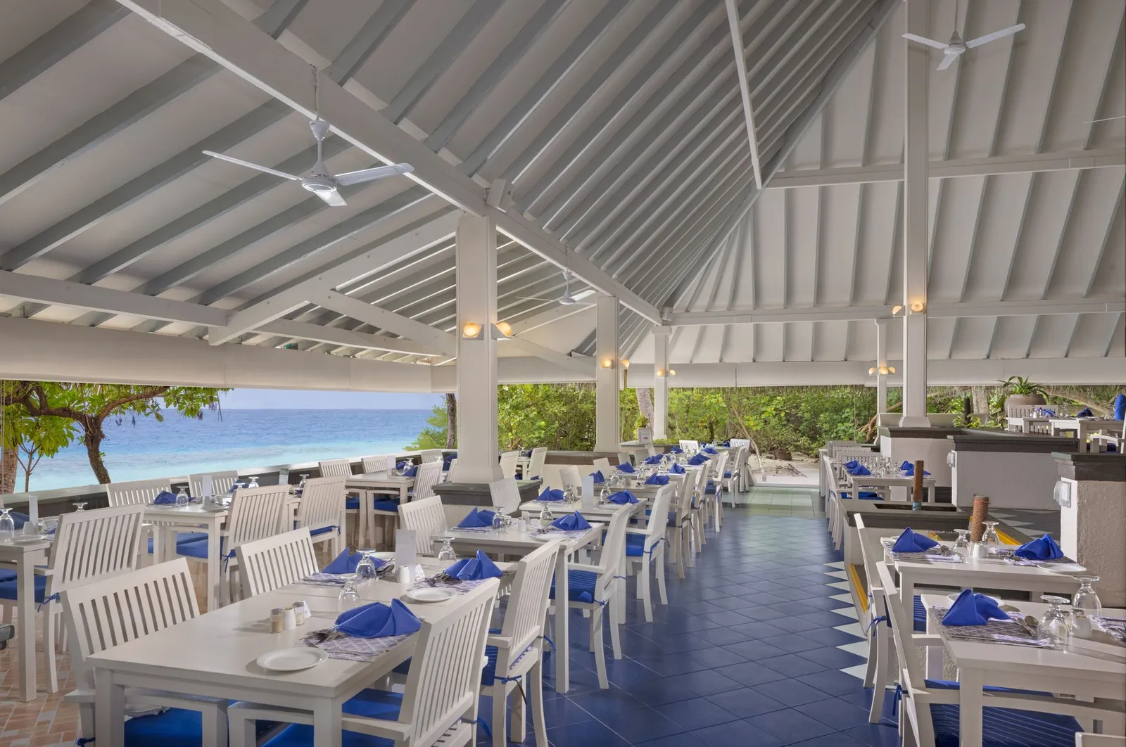The Main Restaurant open to the sea: tables laid in blue under a white beamed roof