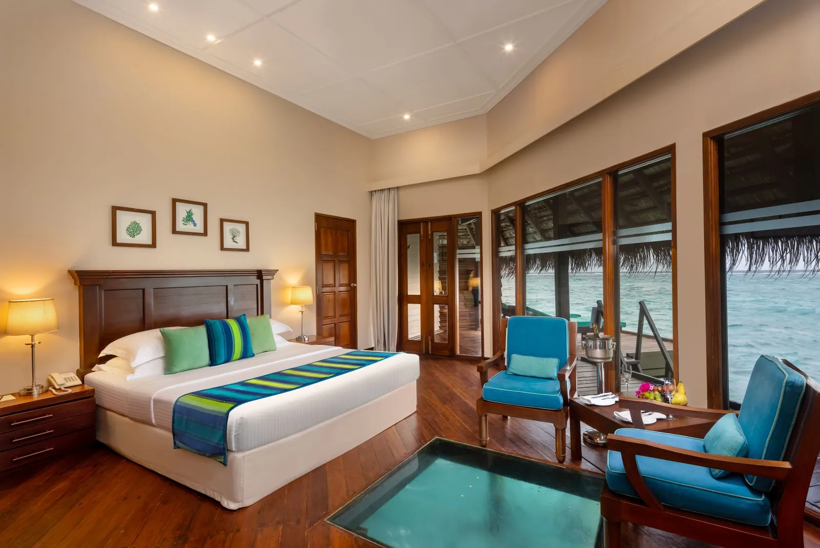 A Sunset Water Villa: the bed, the glass panel in the floor and the windows on the sea