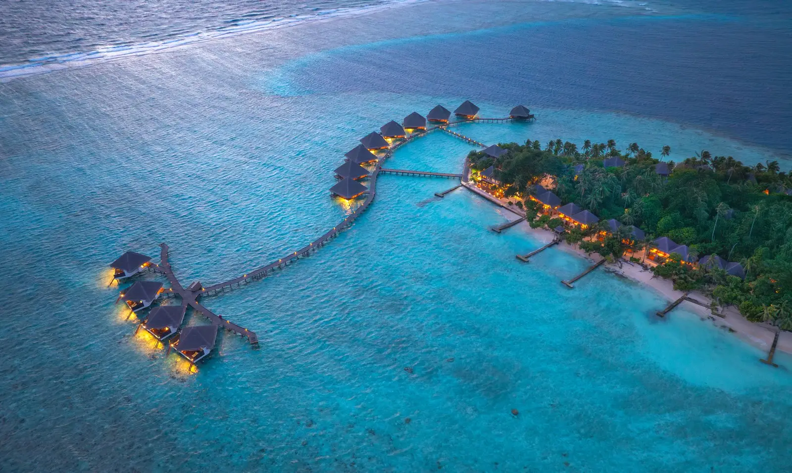 The water-villa jetty at dusk, its lights on above the lagoon