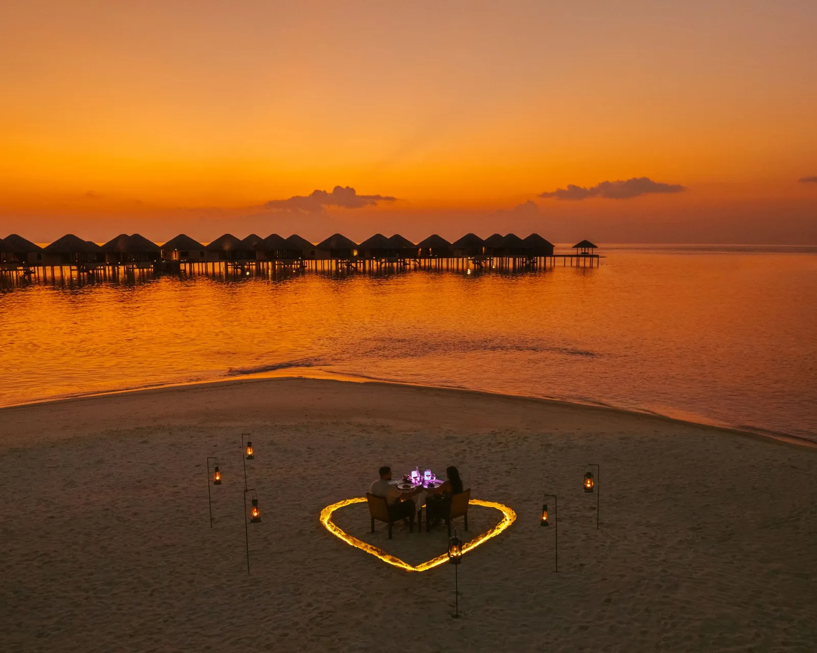 A beach dinner at sunset inside a heart of candles, the villas in silhouette