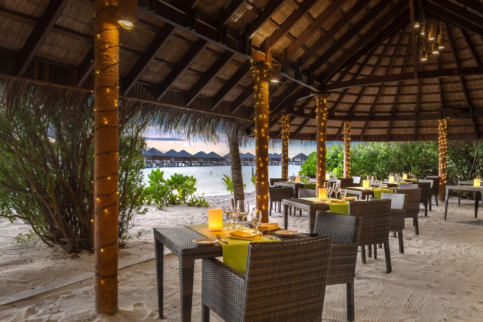 Kakuni in the evening: tables on the sand under the thatch, candles lit