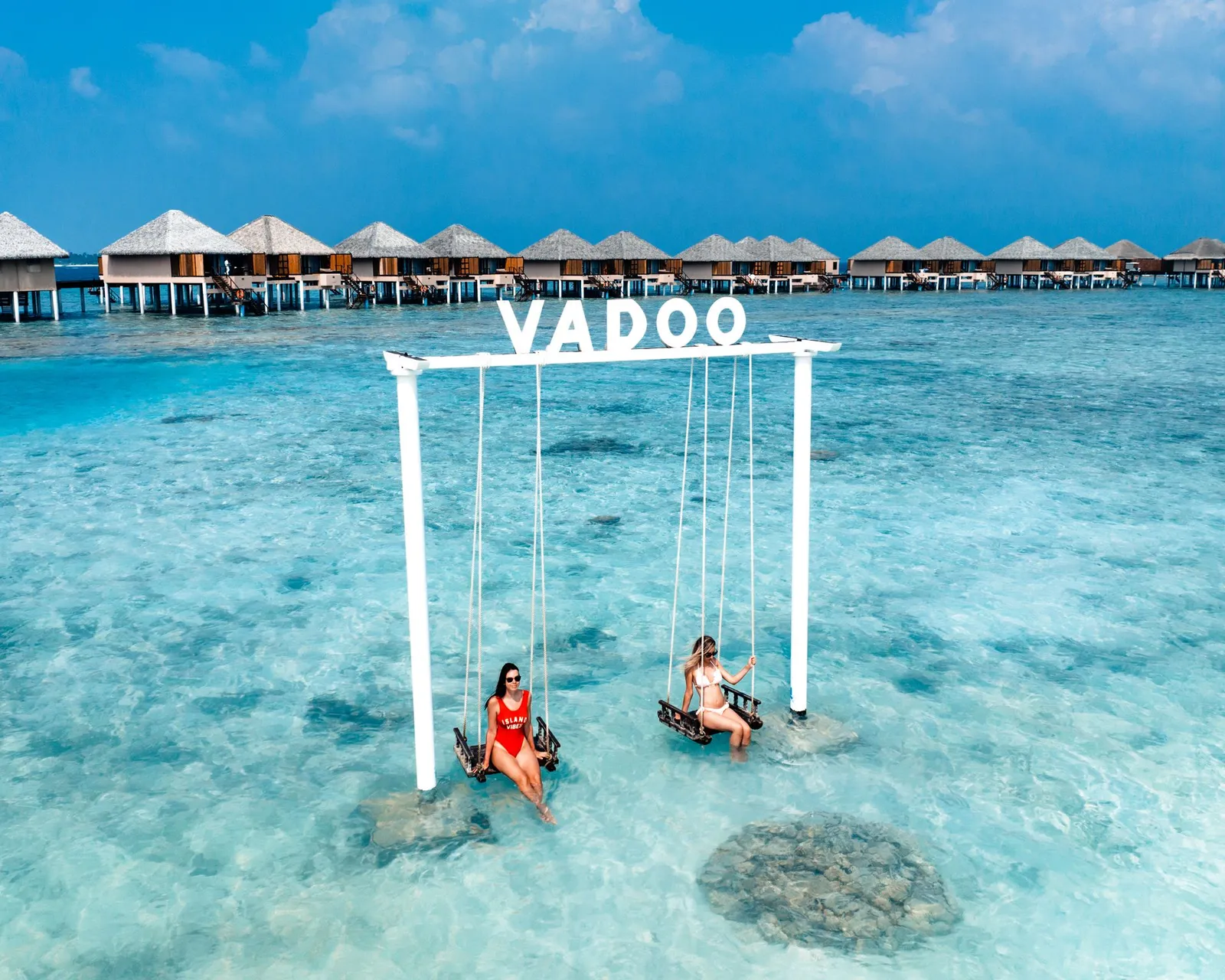 2 people on the VADOO swing in the lagoon, the villas behind