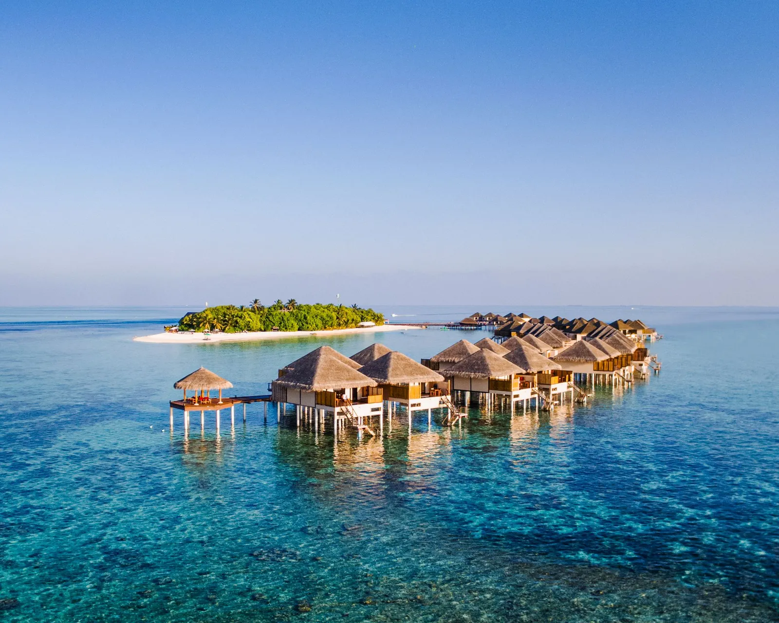 A cluster of water villas over the reef, a green island on the horizon