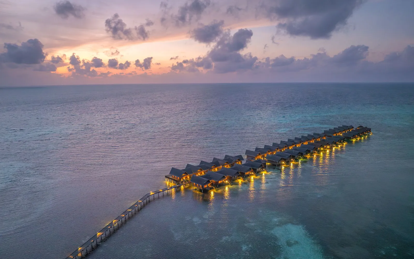 The water villas at dusk, their lights on above the lagoon
