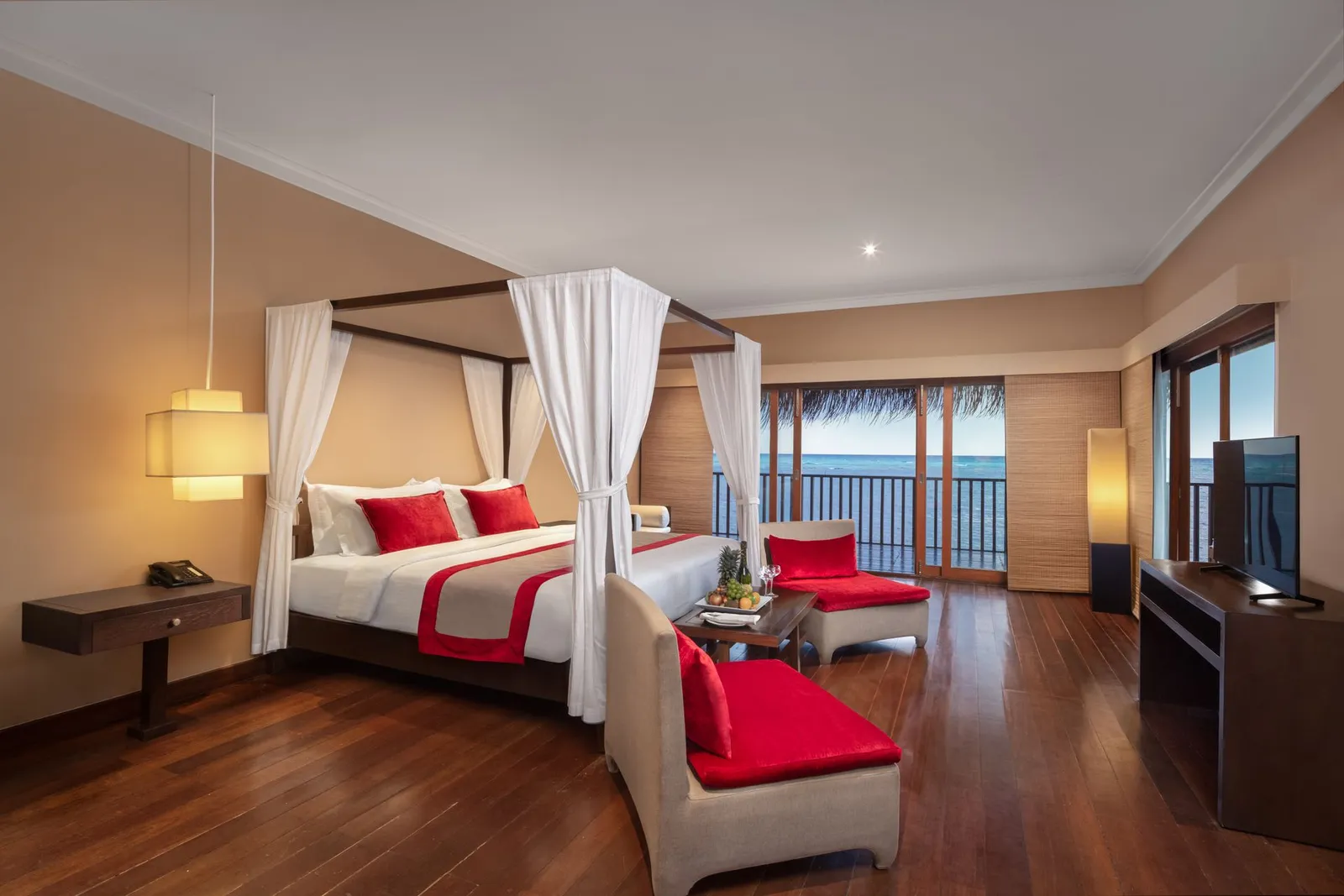 A Sunset Ocean Villa, its canopy bed and red armchairs facing the sea
