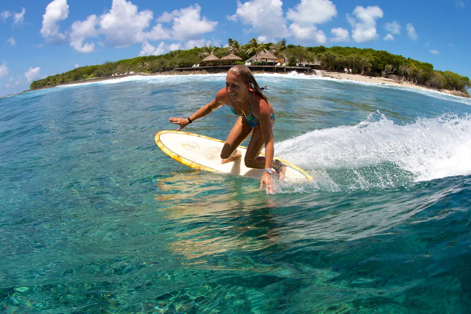 A surfer glides along a wave in front of the island