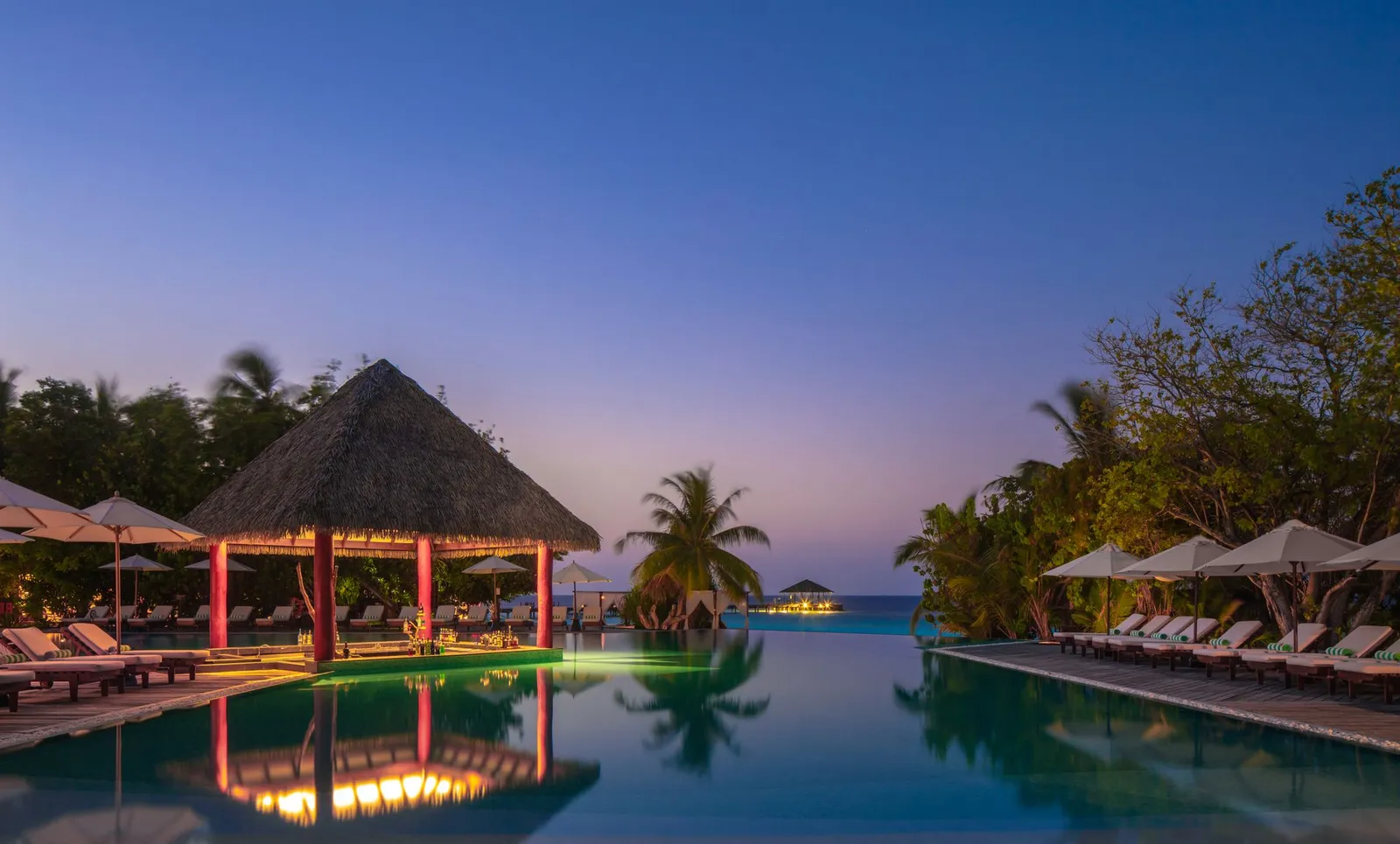 The infinity pool at dusk, the Pool Bar’s pavilion lit and the sea beyond the edge