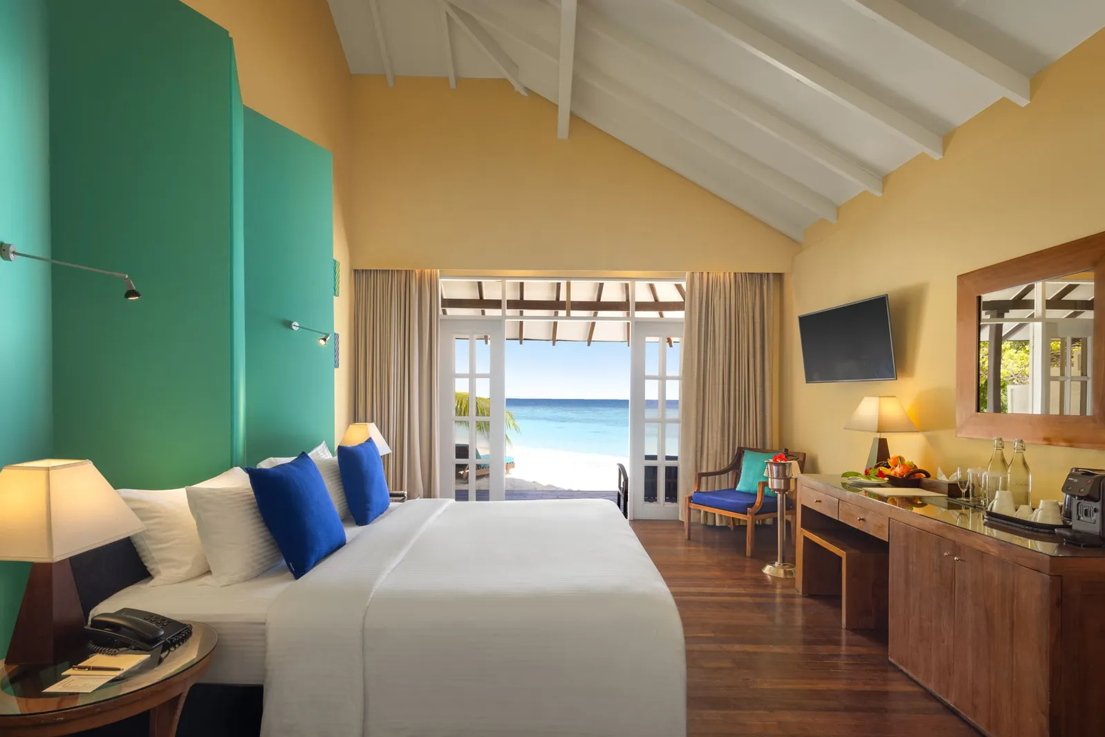 A Beach Villa: the bed with blue cushions, the green wall and the doors open to the beach