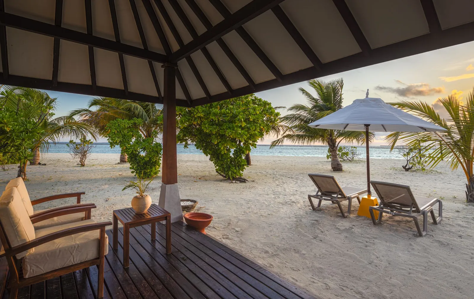 The veranda of a Sunset Deluxe Beach Villa: armchairs, a parasol and loungers on the sand