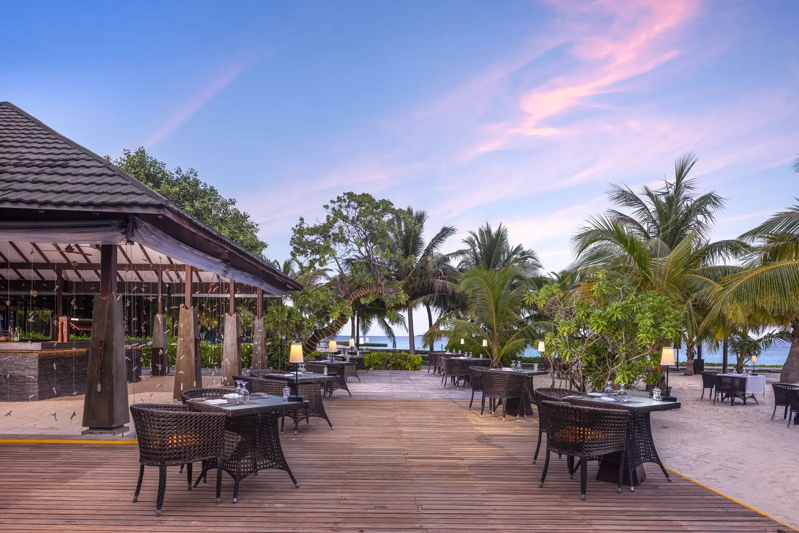 The Thavaa’s deck on the beach at dusk, the tables among the palms