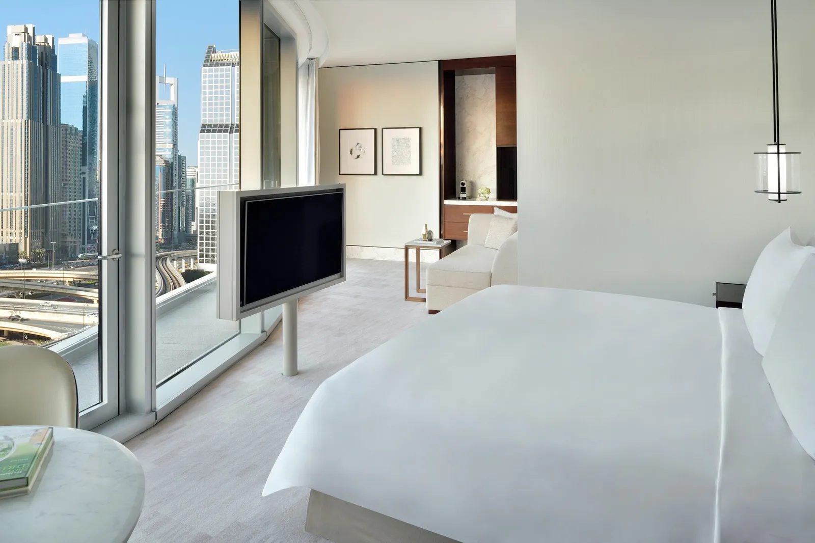 A Premier room with a king bed, a dark-wood bedside table and the city beyond the glass