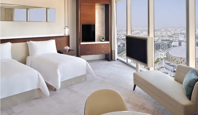 A room with 2 beds, an armchair and pale curtains