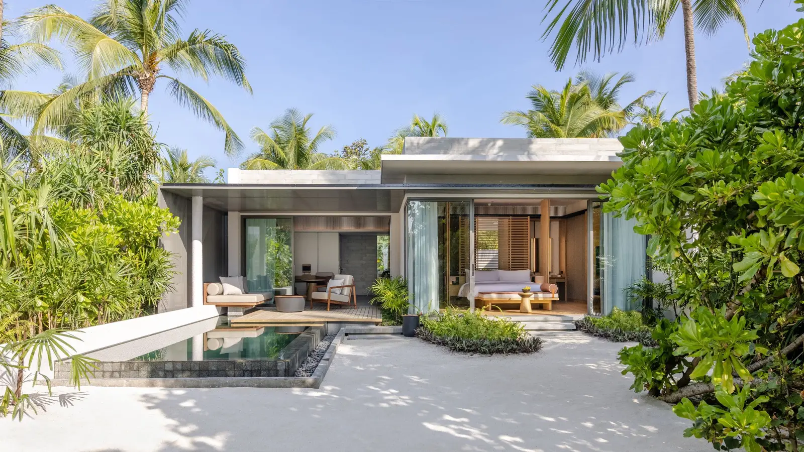 A villa between garden and beach, with glazing and a private pool.