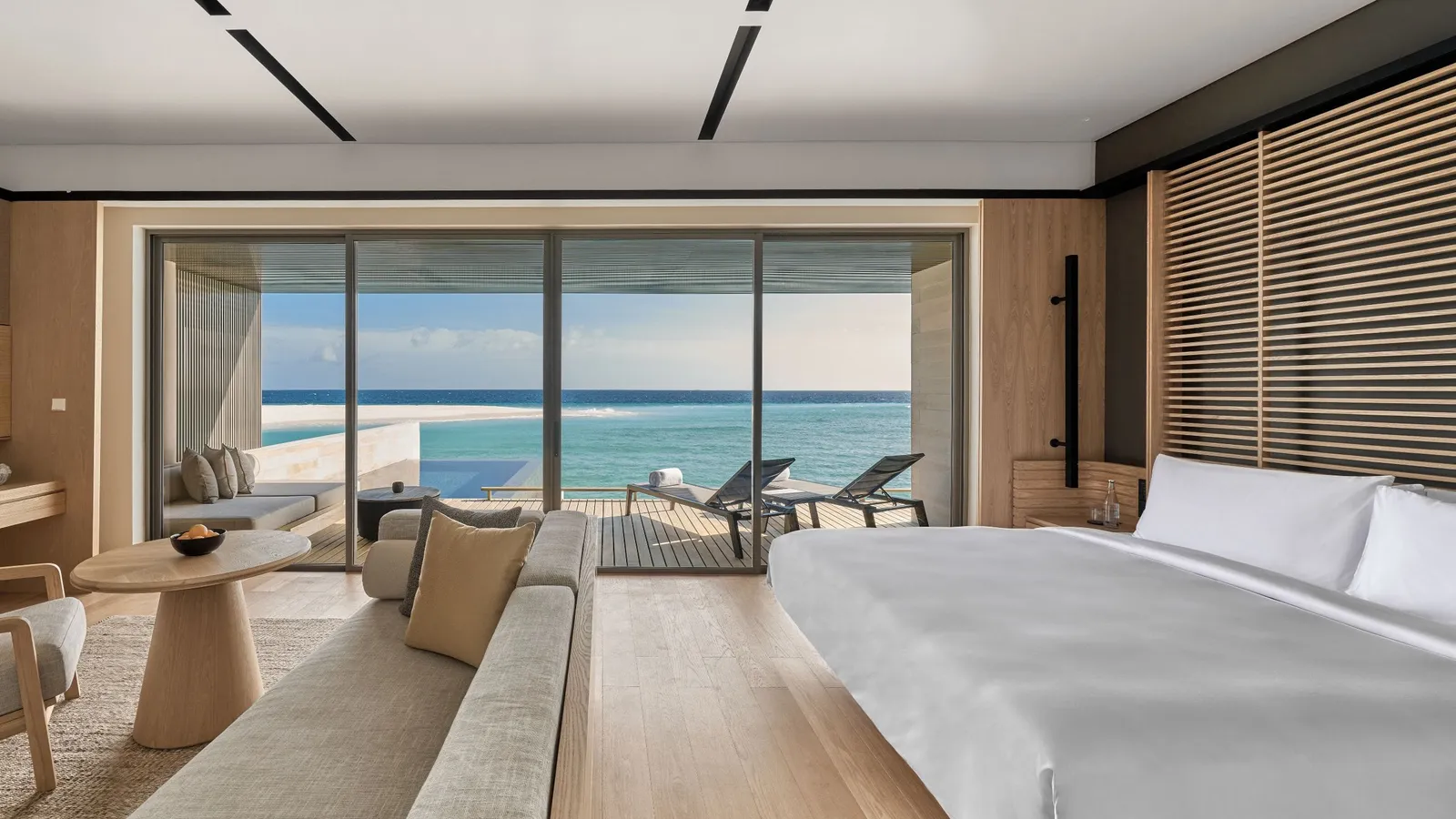 A timber-floored bedroom overlooking the pool and lagoon through glazing.