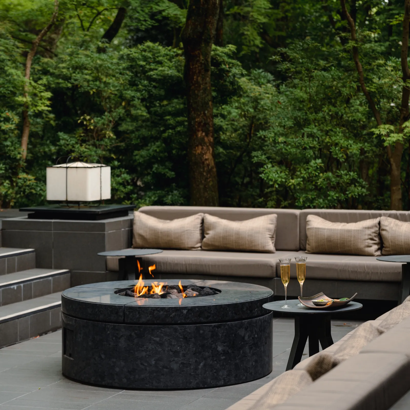 The fire lit in the open-air court, the sofas and 2 flutes of Champagne on a side table, with the forest behind.