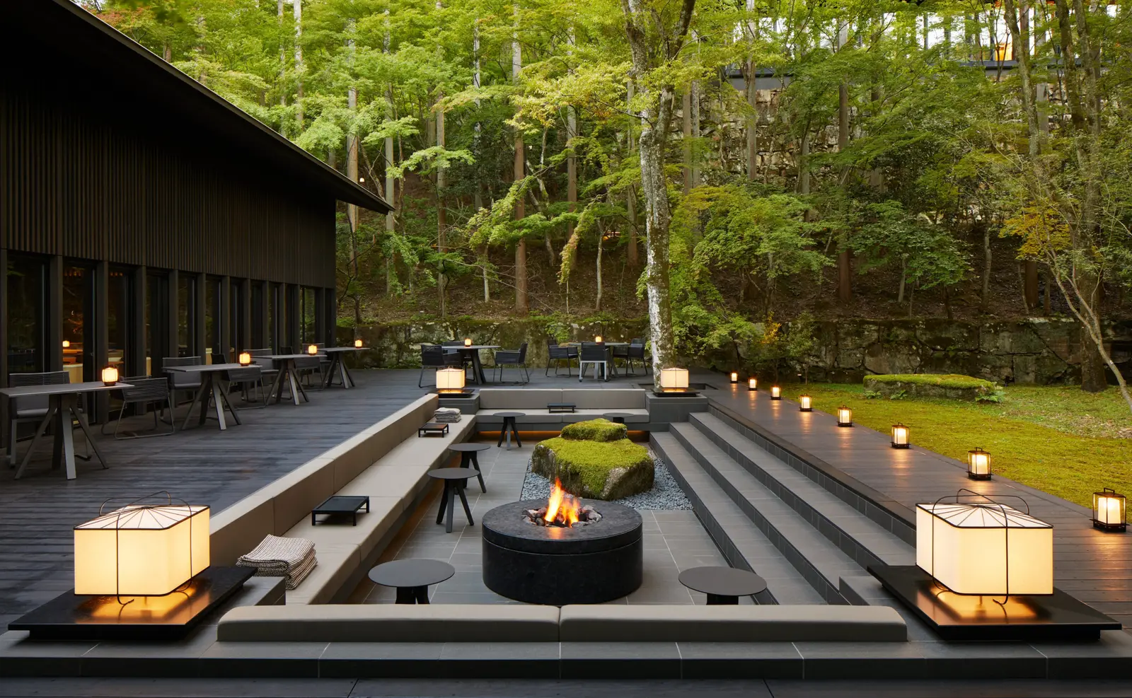 The Living Pavilion’s terrace: the fire lit in the sunken court, paper lanterns on the steps and tables under the forest.