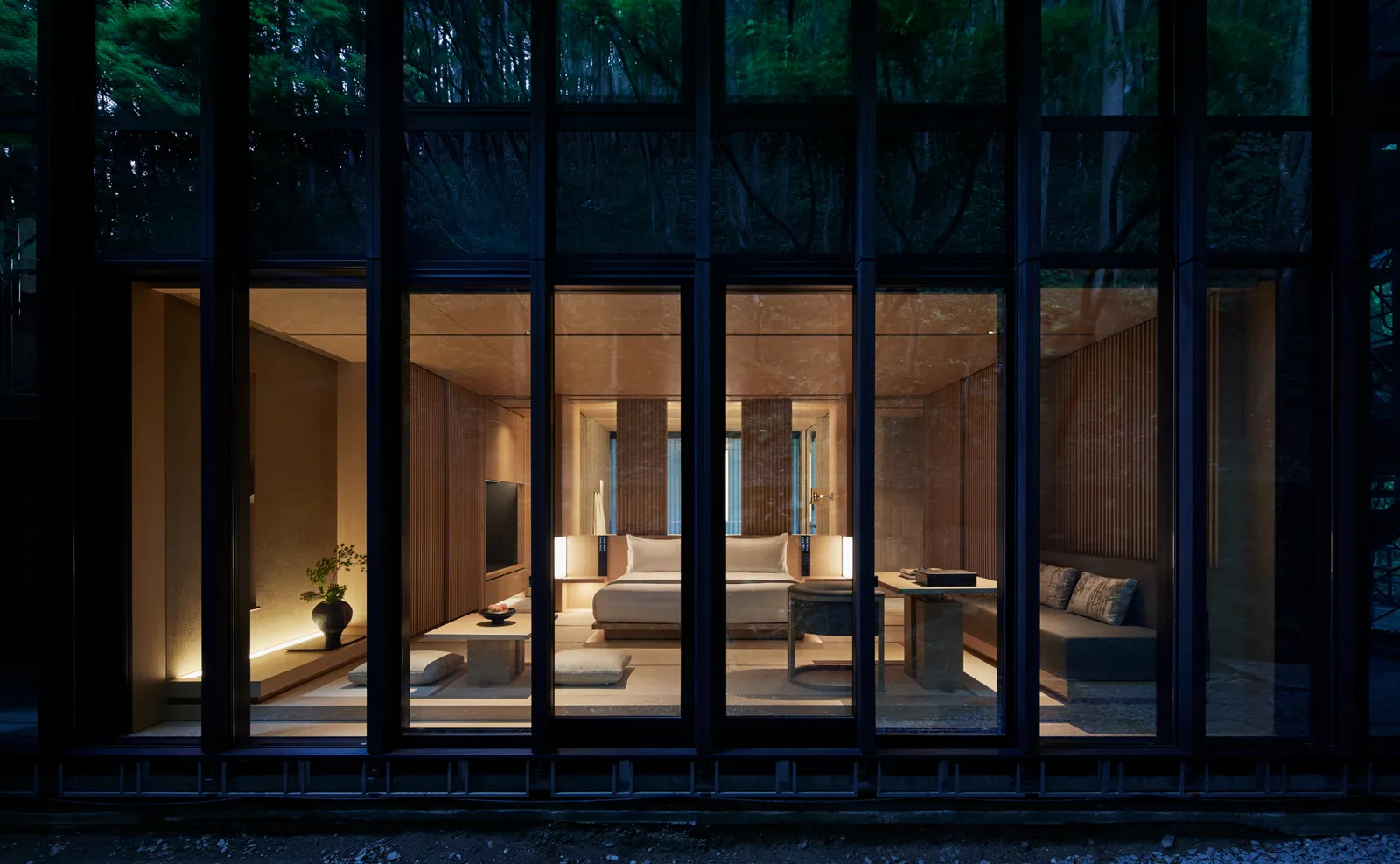 A pavilion lit at dusk seen from the garden through its tall windows: the living room, the tatami and the low lamps.