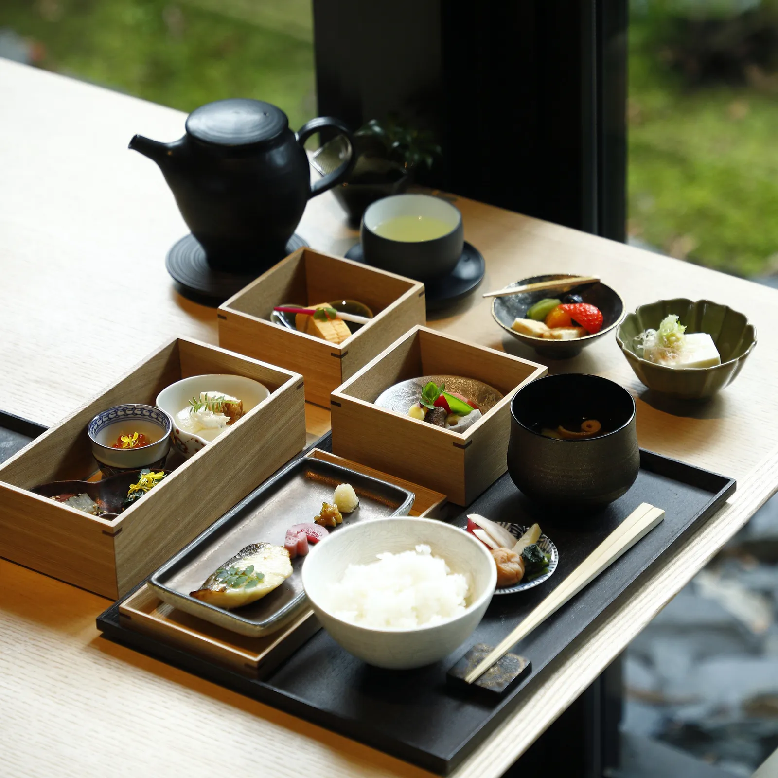 The Kyoto breakfast: wooden boxes of small dishes, rice, miso soup and a black teapot on the tray.