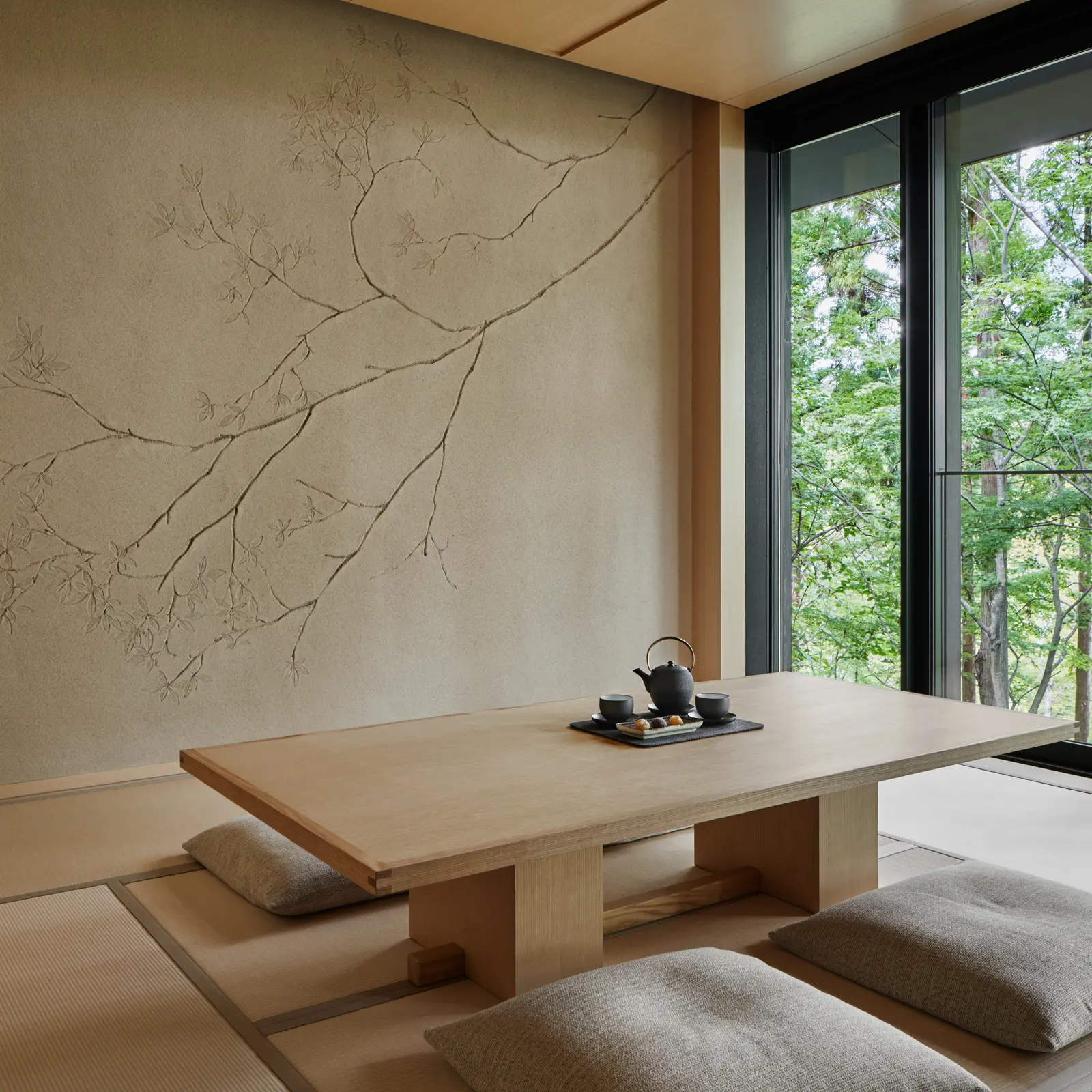 The tatami living room of the Washigamine Pavilion: a low table set for tea, floor cushions and a pale wall with a drawn branch.