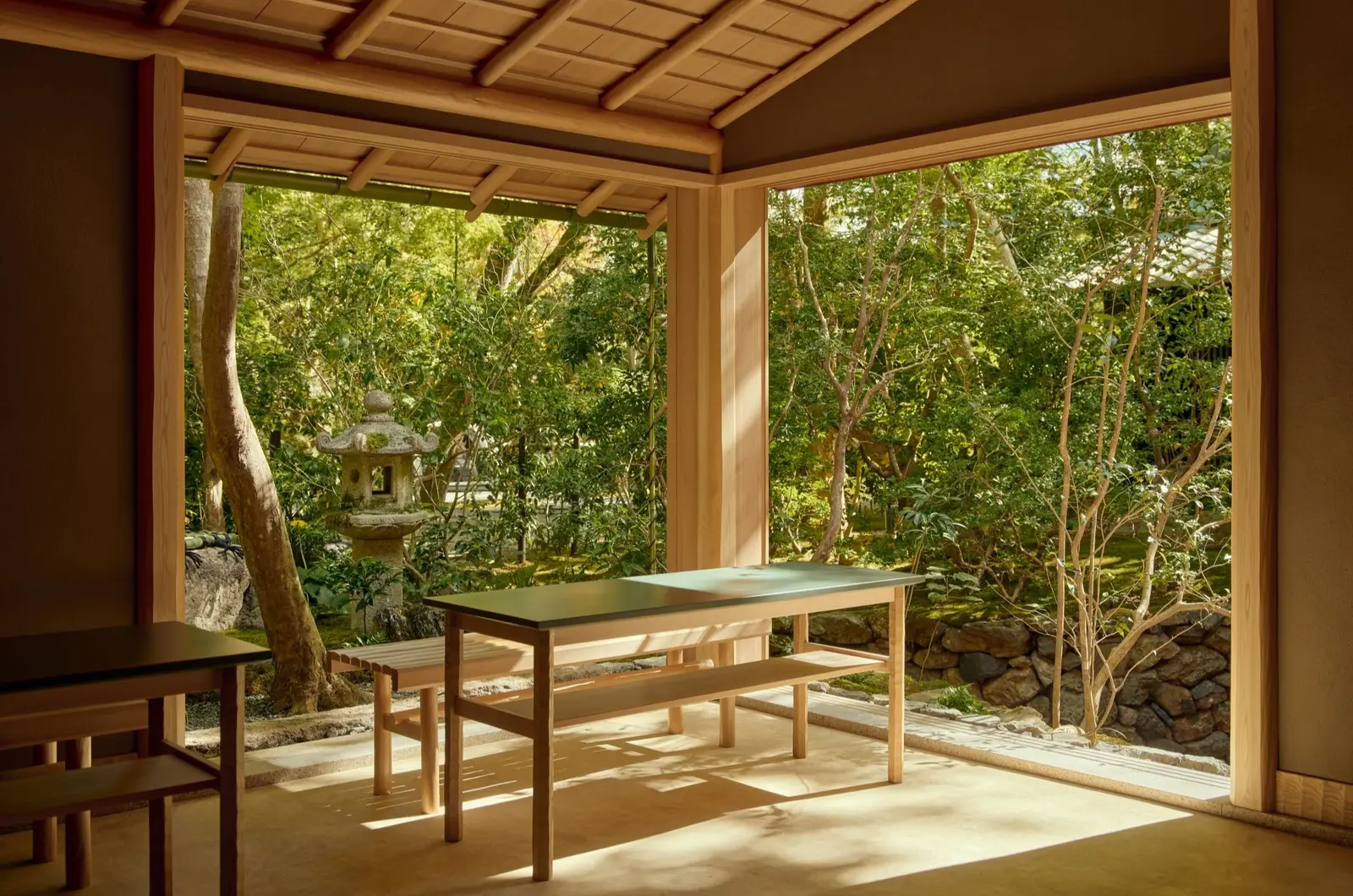 The Ryurei tea room open to the garden, with its wooden table and bench, a stone lantern and the trees outside.