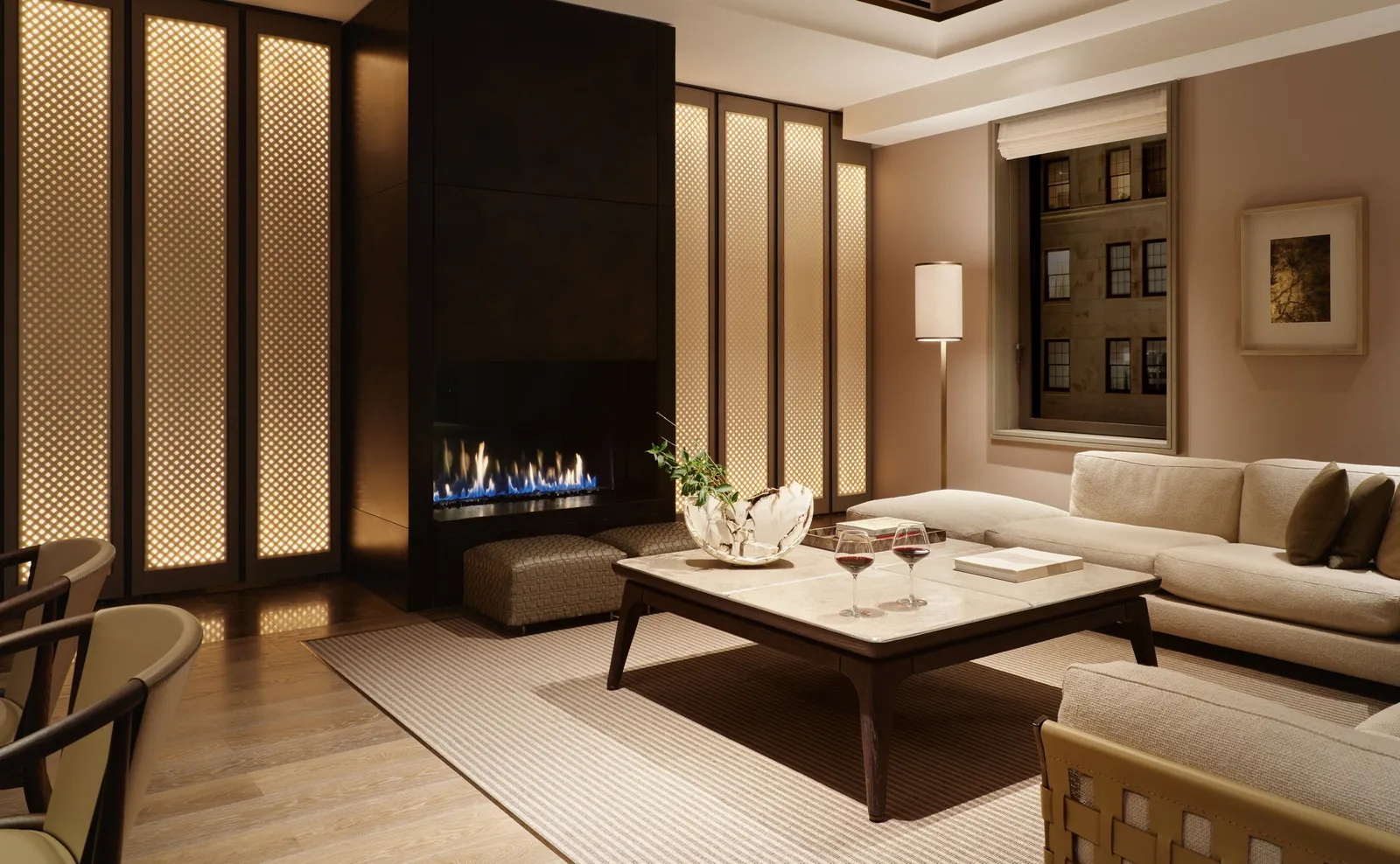A Corner Suite living room in the evening: the fire lit behind glass, pale sofas and low lamps