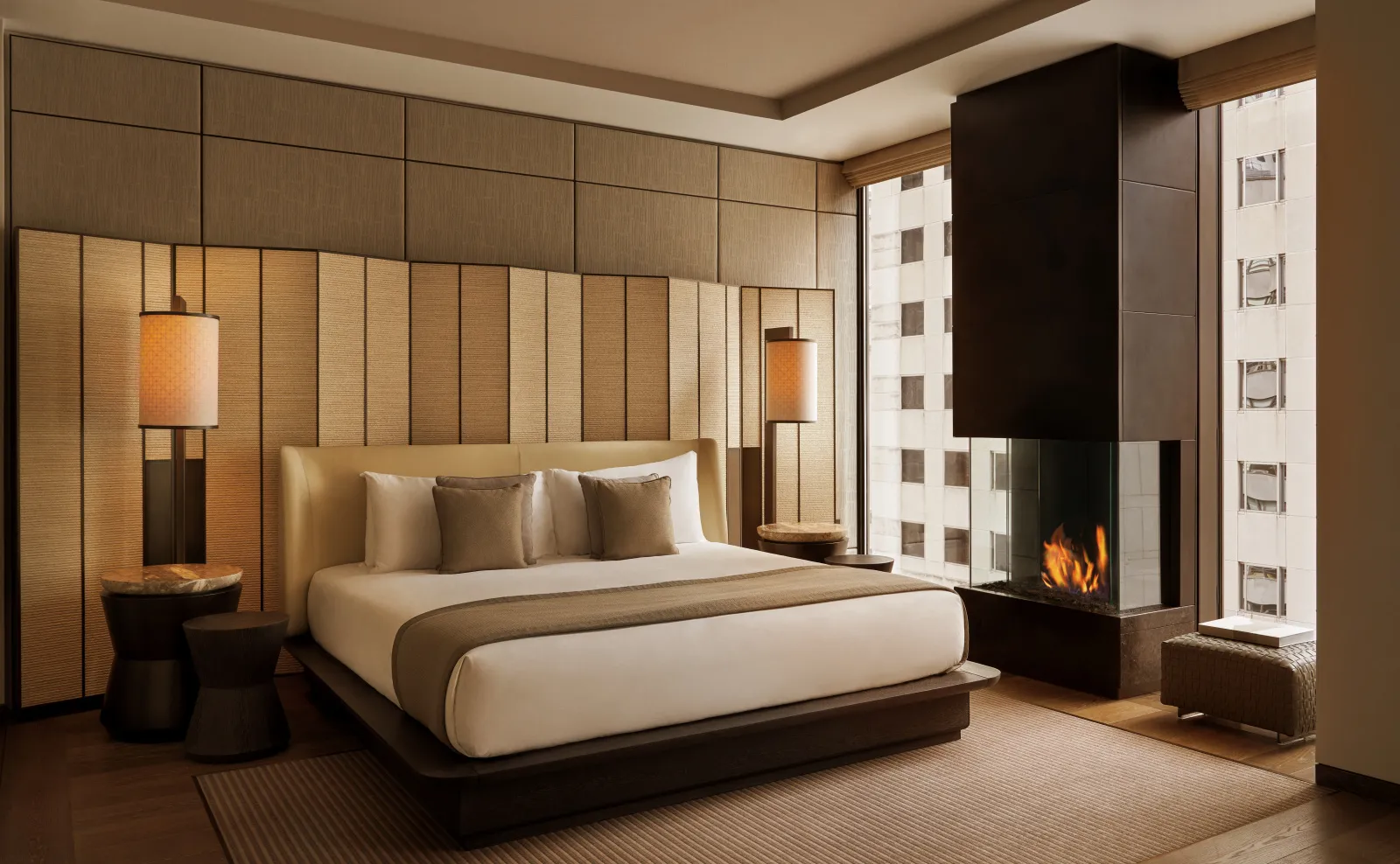 Bedroom at Aman New York with upholstered wall panels, contemporary furnishings, and warm ambient lighting.