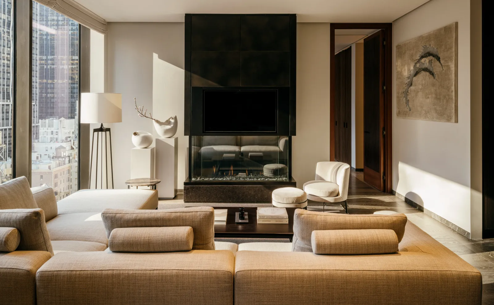 Serene lounge at Aman New York with neutral seating, fireplace, and floor-to-ceiling windows overlooking the city.