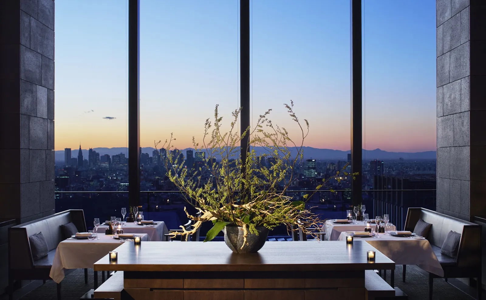 Arva’s laid tables before the windows, a large vase of branches in the middle and the skyline at sunset.